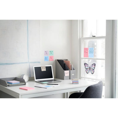 A tidy office desk with a laptop, clock, notepad, file folder, and 3M Deutschland GmbH Post-it® Super Sticky Notes (47.6x47.6 mm, 90 sheets/block, 100% PEFC). Next to the desk is a window with butterfly decoration and pastel-colored sticky notes.