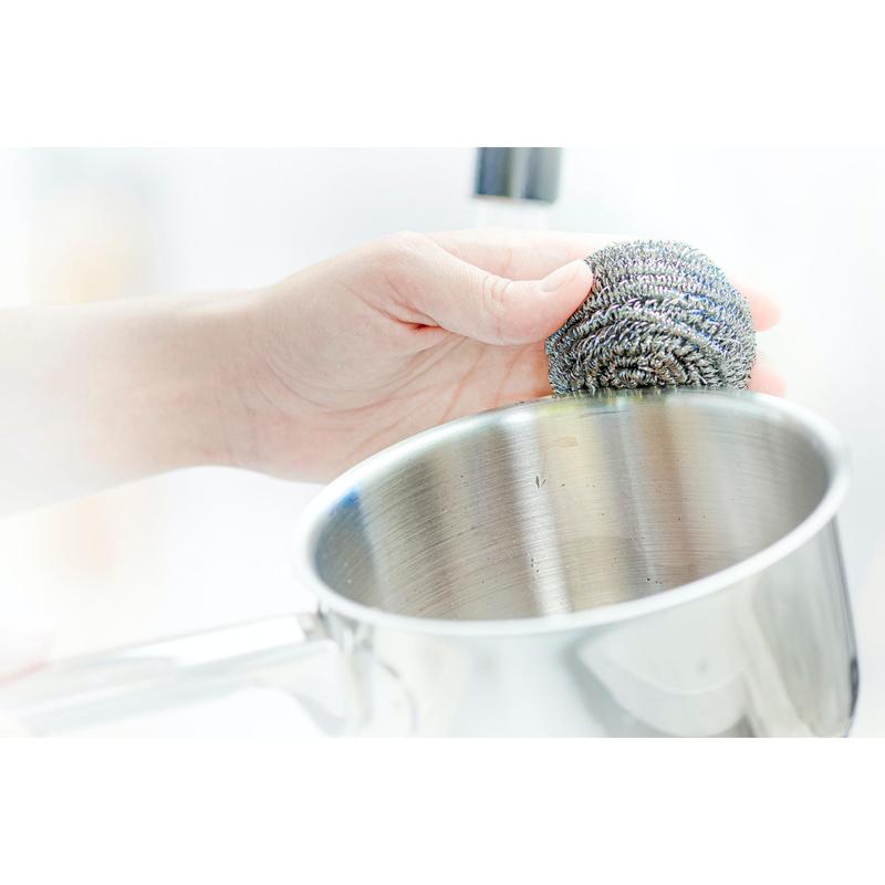 A person uses a Scotch-Brite® stainless steel spiral scrubber from 3M Deutschland GmbH—3 per package—to remove stubborn stains while cleaning a stainless steel pot.