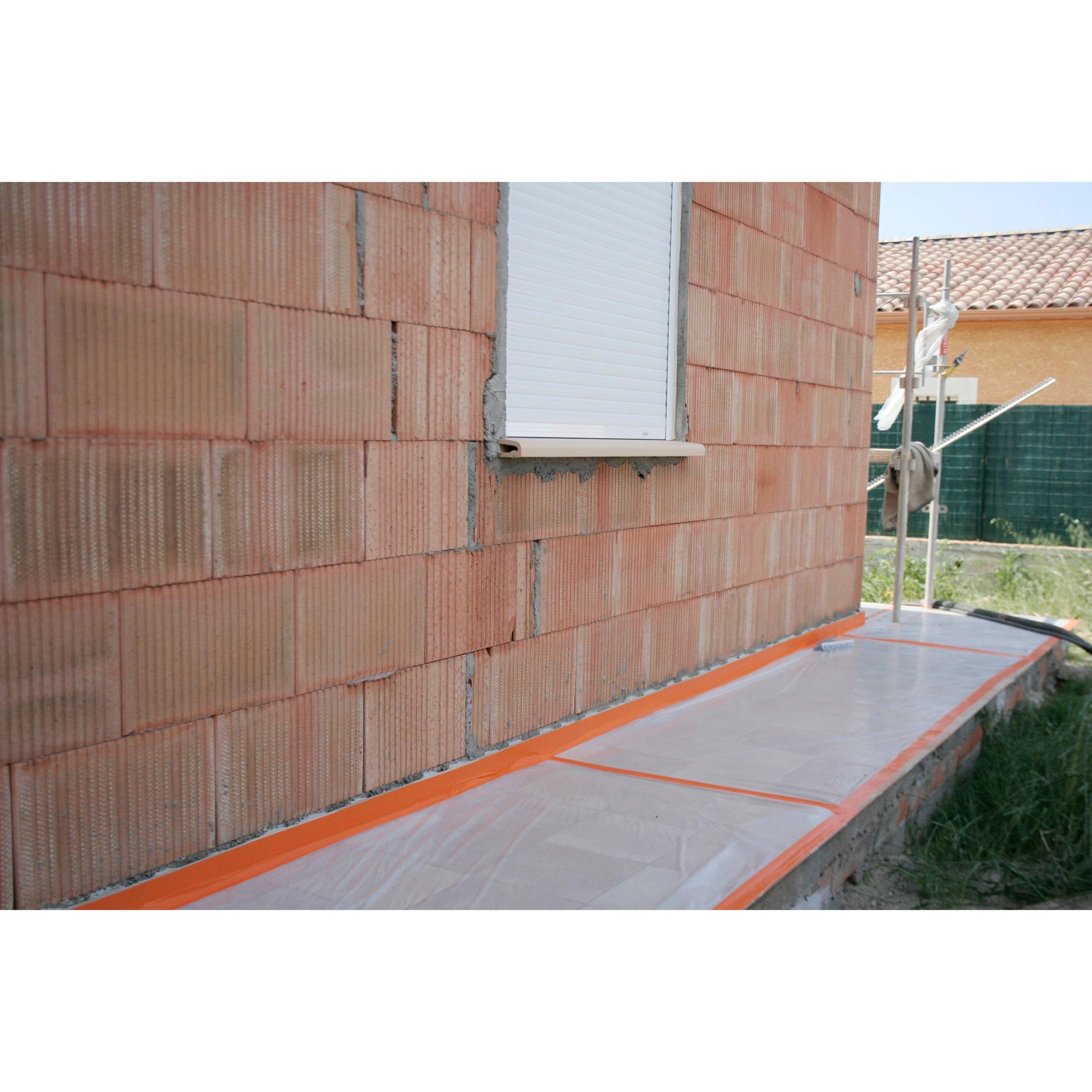Eine gemauerte Außenwand mit einem geschlossenen weißen Fensterladen. Der Boden ist mit Kunststofffolien bedeckt, die mit Scotch® High Visibility Klebeband, orange, 25 m x 48 mm von 3M Deutschland GmbH gesichert sind, wahrscheinlich für Bau- oder Malerarbeiten.
