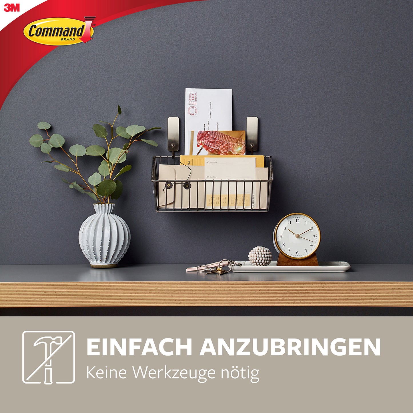 Ein mittelgroßer Command™ Metallhaken in gebürstetem Nickel von 3M hält einen Drahtkorb an der dunklen Wand - ganz ohne Bohren. Ideal für Post und kleine Gegenstände. Einfach anzubringen, keine Werkzeuge nötig.