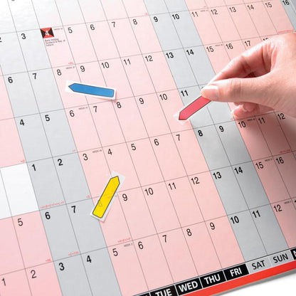 A hand places a red Post-it® Index Arrow (11.9 mm x 43.2 mm) from 3M Deutschland GmbH on a calendar, blue and yellow arrows mark other appointments on the black-printed, pink and gray background. Each dispenser contains 100 sticky notes.
