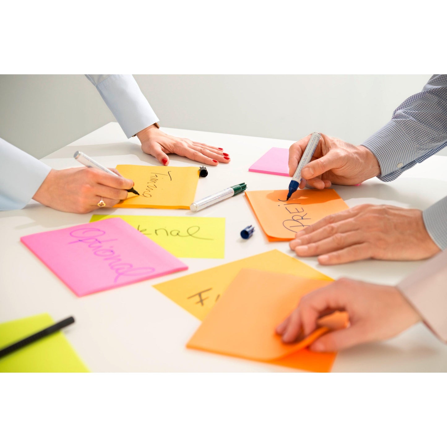 Drei Personen schreiben auf 3M Post-it® Super Sticky Meeting Notes in verschiedenen Neonfarben (203 x 152 mm, 45 Blatt/Block, 4 Blöcke/Packung), 100% PEFC zertifiziert. Auf den leuchtenden Haftnotizen sind nur Hände und Arme zu sehen, wenn Worte geschrieben werden.