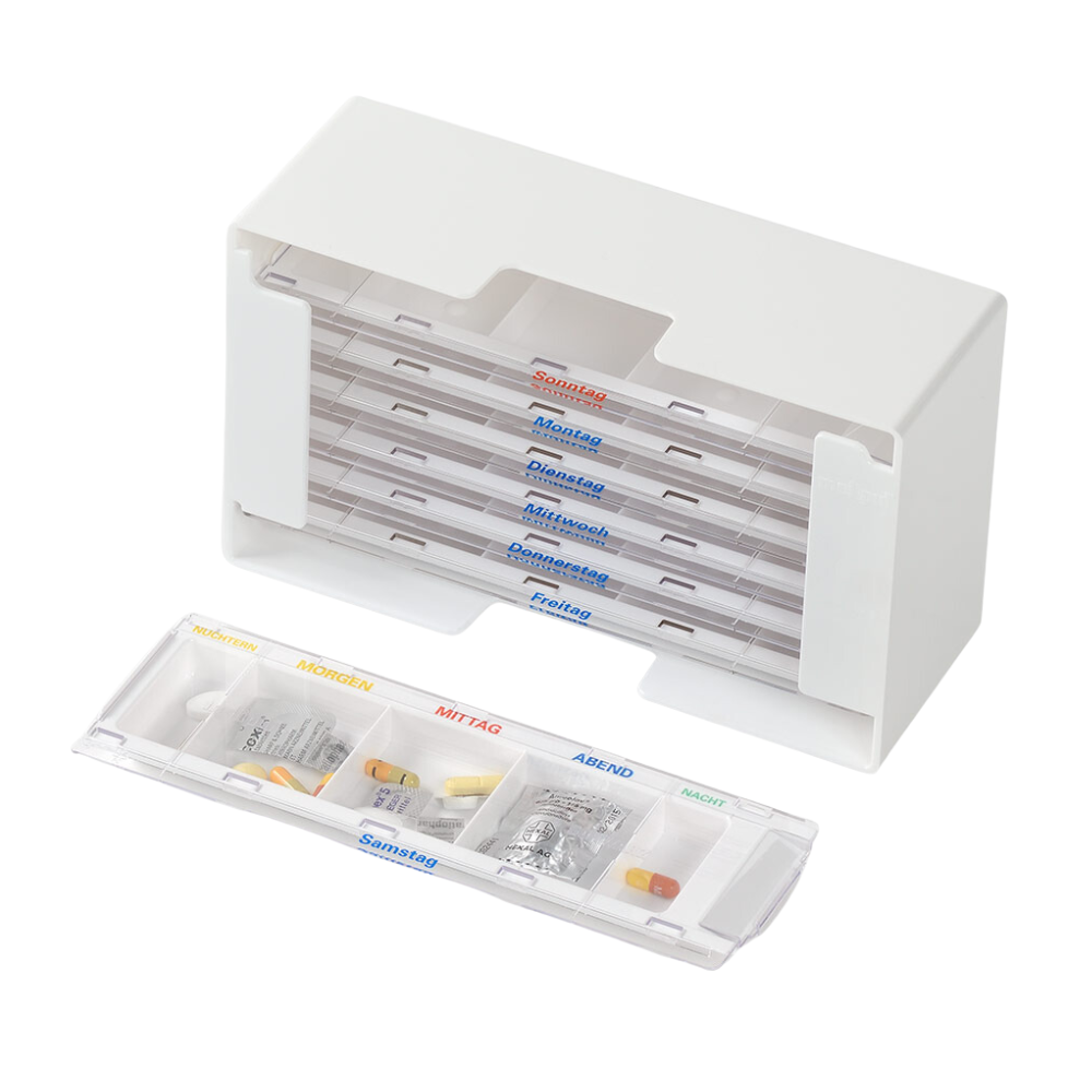 A white melipul medication dispenser XL-5 by Helmut Schwarz GmbH, with a week's supply of tablet containers labeled in German for morning, noon, and evening doses. One container is retractable and displays various tablets in individual compartments.